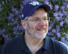 Andy Becker in front of a wall of flowers, wearing a baseball cap. 
